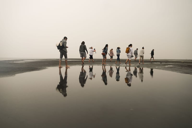 Visitors to Silver Sand Beach at the Great Salt Lake Marina are reflected on still water as they walk during a rainstorm.